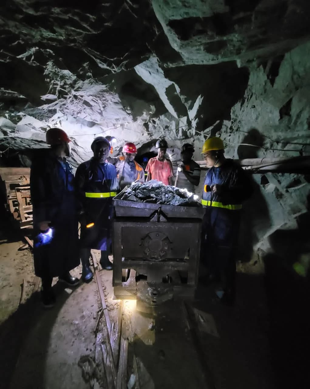 Underground mine workers in safety helmets gathered around an ore cart at a Gengetatu Extech shaft